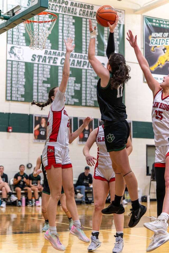 A basketball player rising for a jump shot over two defenders in a packed gym