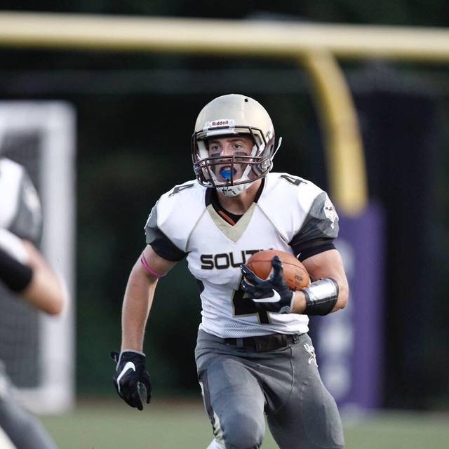 A football player in full pads sprinting upfield with the ball tucked