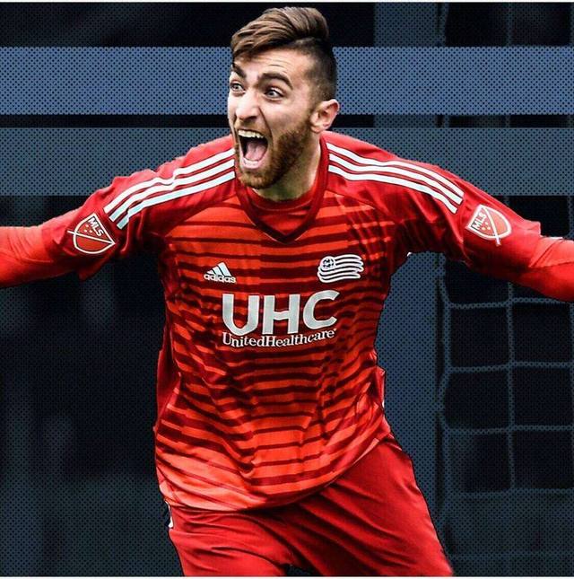 Matt Turner in a New England Revolution kit, arms spread wide, roaring after a save