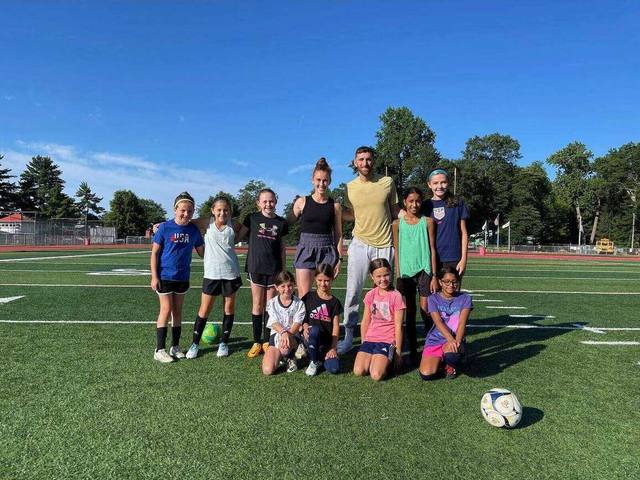 Ryan Nie and a fellow coach on a sunlit turf field with a group of young soccer players