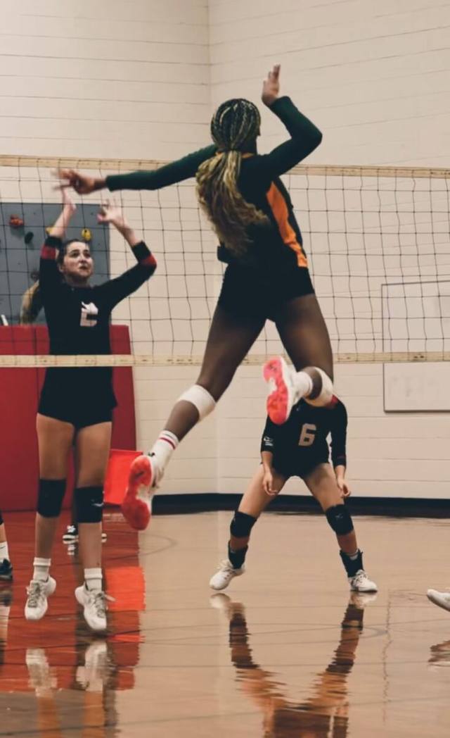 A volleyball player high above the net, arm cocked to spike